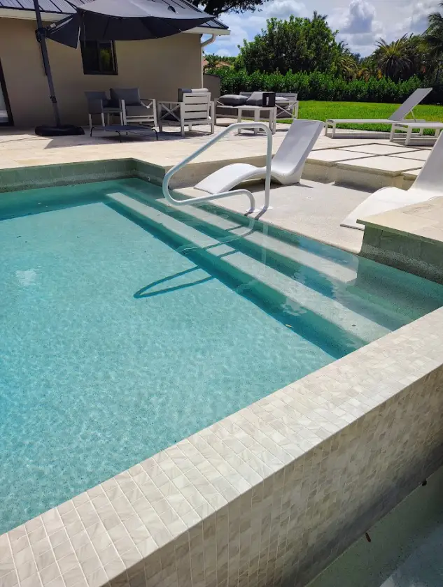Pool entry steps with a handrail, a light interior finish, and tile on the raised wall of a South Florida pool