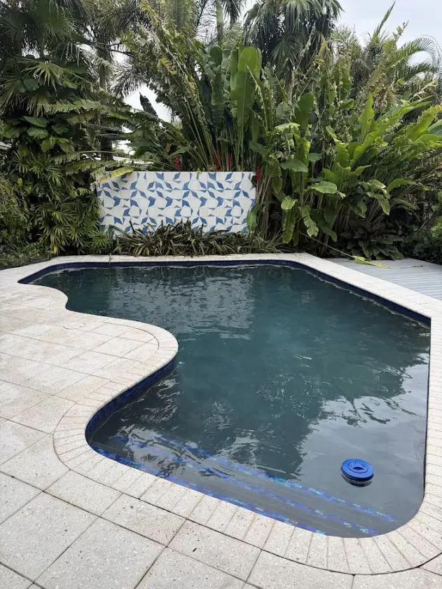 Freshly resurfaced Boca Raton pool with a deep, dark pebble interior finish and travertine coping
