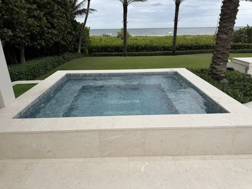 Oceanfront Palm Beach County spa finished in gray glass mosaic tile with travertine coping, steps from the Atlantic