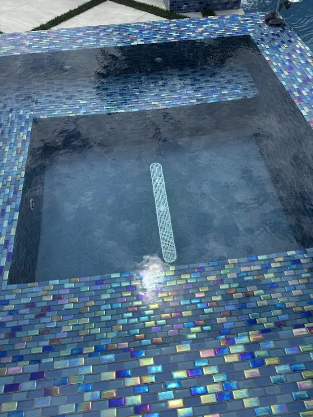 Close-up of a Boca Raton pool finished in iridescent blue glass mosaic tile over a dark pebble interior