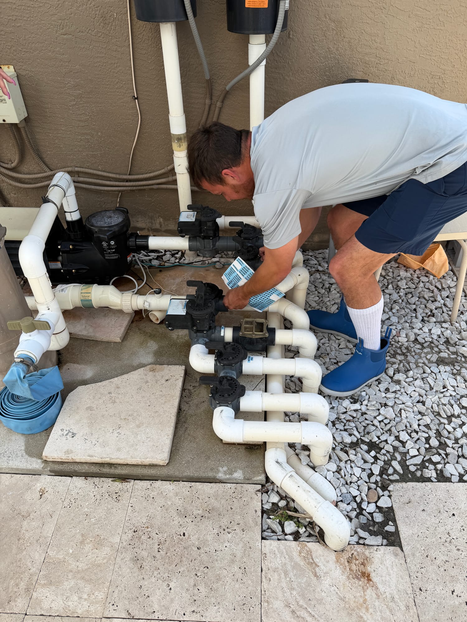 A Florida's Best Pools technician working on a residential pool equipment pad — diagnosing a pump/manifold issue on a Delray Beach route